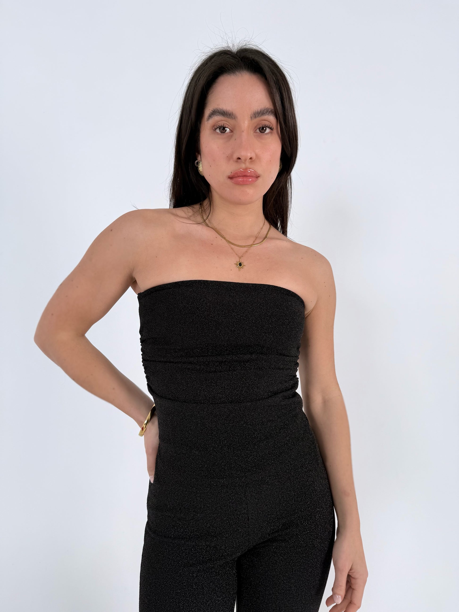 Woman wearing a black strapless glittered top and pants against a white background