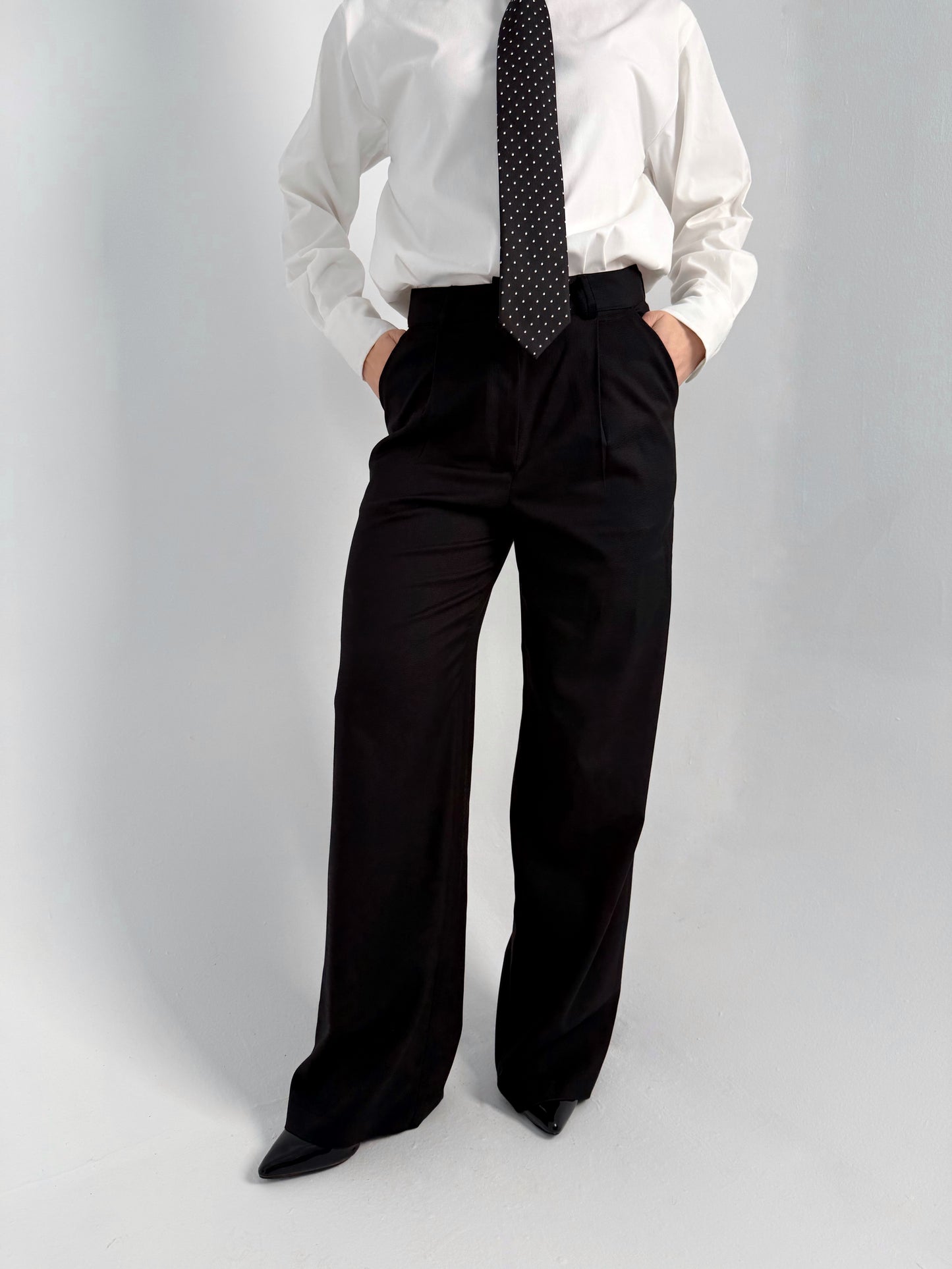 women wearing a white shirt, black tie, and black wide-leg pants on a gray background