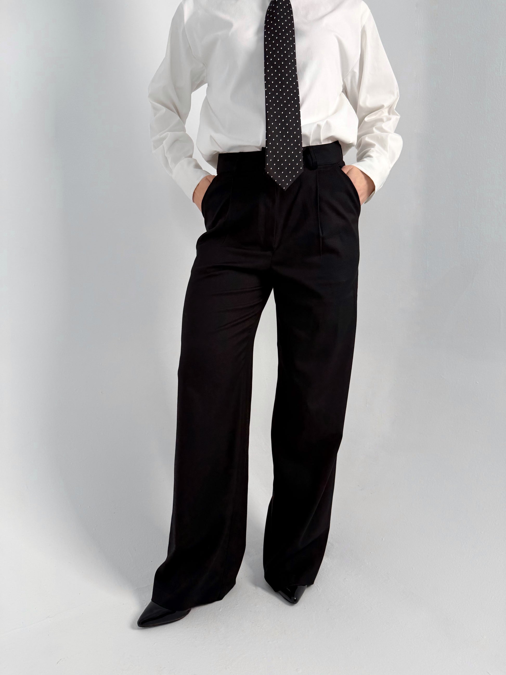 women wearing a white shirt, black tie, and black wide-leg pants on a gray background