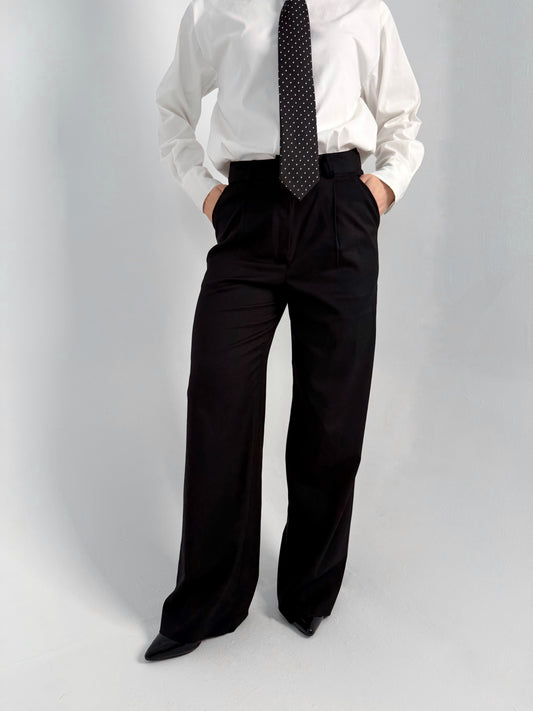women wearing a white shirt, black tie, and black wide-leg pants on a gray background